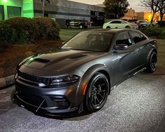 a gray car parked in front of a parking lot at night with other cars behind it