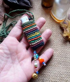 a hand holding a small cell phone case made out of beads and other things on the table