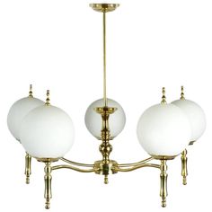 an antique brass chandelier with five white glass globes hanging from the ceiling