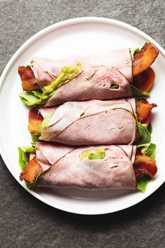 ham roll ups on a white plate with lettuce and bacon in the middle