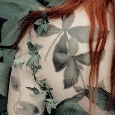 the back of a woman's body covered in leaves and ivys with red hair