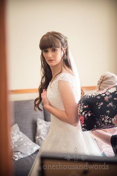 a woman standing in front of a mirror wearing a wedding dress and holding her hands behind her back