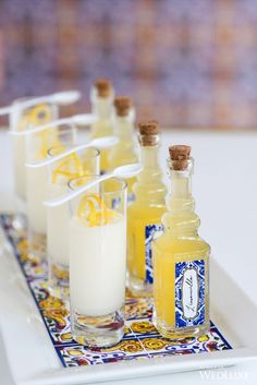 several bottles and glasses filled with liquid on a tray next to another glass full of liquid