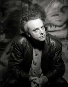 a black and white photo of a man in a leather jacket with his hands on his knees