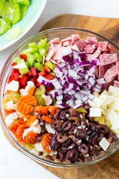 chopped vegetables and diced meat in a bowl on a cutting board next to a salad