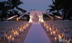 an outdoor wedding setup with white drapes and lit candles on the aisle leading into the ceremony