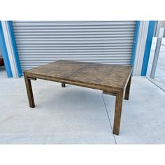 a wooden table sitting on top of a cement floor next to a blue and white building