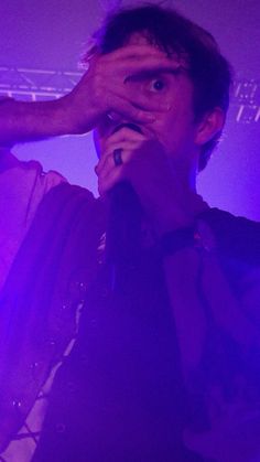 a man holding his hand up to his face while standing in front of a purple light