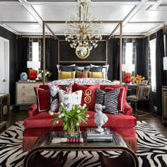 a red couch sitting in front of a bed next to a table with a vase on it