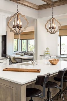 a kitchen island with stools and lights hanging from it's ceiling in front of windows