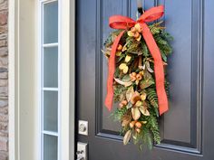 a wreath hanging on the front door of a house with an orange bow and berries