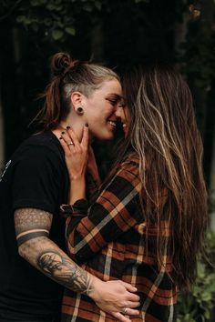 two young women hugging each other in the middle of an outdoor area with trees and bushes behind them