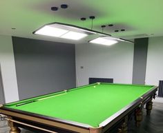 a green pool table in an empty room with two lamps on the ceiling and several chairs around it