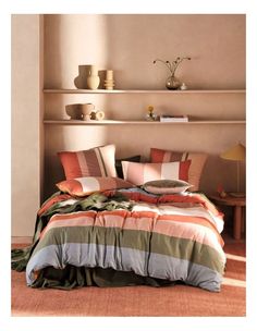 a bed with many pillows and blankets on top of it in front of a shelf