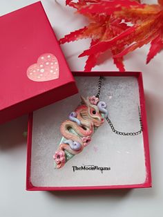 a pink box with a necklace in it next to a red plant and some leaves