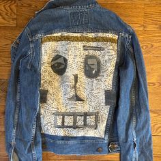 a denim jacket with an image of a face on the front and back, sitting on top of a wooden floor