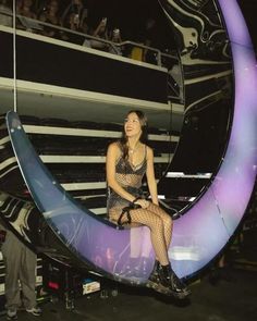 a woman sitting on top of a crescent moon in the middle of a stage with people watching