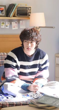 a person sitting on a bed reading a book and looking at the camera while wearing a striped sweater