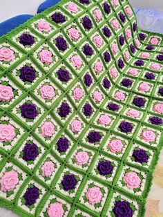 a crocheted blanket with pink and purple flowers on it sitting on a bed