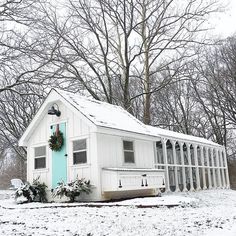 a small white house with a blue door and wreath on it's side in the snow