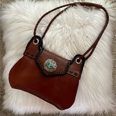 Charming Small Shoulder Bag With Adjustable 48” Long Strap. Inside Divider, Back Pocket. 117 Inches. Two-Toned: Rich Brown Leather With Black Accents. This Version Has The Silver Charm Concho And Turquoise Accent. This Is New/Never Used. Received As Gift And It’s Not My Style (But It Is Gorgeous!). Western Bags With Concho Detail, Western Style Bags With Concho, Western Hand Tooled Bags For Daily Use, Western Hand-tooled Bag For Daily Use, Western Style Hand-tooled Bag For Daily Use, Southwestern Brown Rectangular Shoulder Bag, Brown Southwestern Rectangular Shoulder Bag, Southwestern Style Brown Rectangular Shoulder Bag, Western Leather Shoulder Bag For Everyday Use