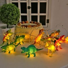 small dinosaur string lights sitting on top of a table next to a cake and potted plant