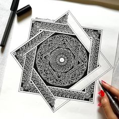 a woman's hand is holding a pen and drawing an intricate design on paper