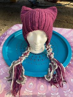 a knitted cat hat on top of a plastic blue plate with tassels