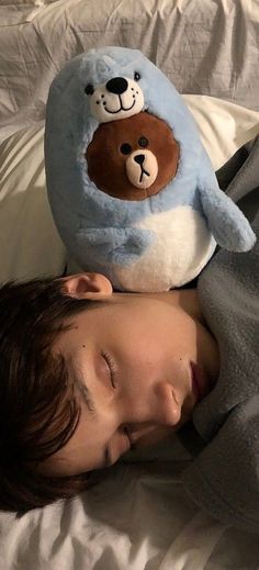 a young boy sleeping next to a stuffed animal