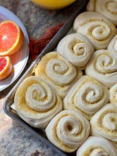 a pan filled with cinnamon rolls next to sliced oranges