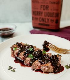 a white plate topped with meat covered in sauce and garnished with green leaves