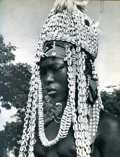 an african woman with braids and beads on her head, standing in front of trees