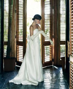 a woman in a white dress is standing by some shutters