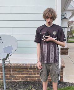 a young man standing in front of a house holding a black cat and looking at his cell phone