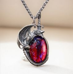 Embrace your inner strength and mythical allure with this stunning handcrafted dragon necklace. The dragon, made of 925 sterling silver, wraps protectively around a mesmerizing "Dragon's Breath" stone, which shimmers with an otherworldly mix of fiery reds and deep purples, reminiscent of mystical flames. The intricate detailing of the silver dragon captures its fierce yet elegant nature, and the sword behind the dragon adds an element of bravery and protection. The necklace hangs from a durable titanium chain, ensuring lasting quality and comfort.  This unique piece is perfect for fantasy lovers, dragon lover, or anyone looking to add a touch of magic to their jewelry collection. Material: Pendant: Sterling silver(dragon), dragon breath glass Chain: 22 inches titanium Silver Dragon Necklace, Jewelry Purple, Dragon Bracelet, Dragon Lover, Dragon Necklace, Magical Jewelry, Crystal Opal, Silver Dragon, Dragon Pendant