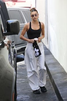 a woman in white pants and black tank top walking down the street with her handbag