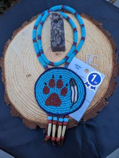 Handmade by me, an Indigenous woman: each of my pieces are individually made depending on what I am feeling when I start a piece.  This beaded "Wolf Spirit" wolf paw print necklace with eagle feather will turn heads when you have it on. Made with two shades of turquoise seed beads, and a brick wolf paw print with an eagle feather next to the print. Beaded on real leather. Neck strand is made with wrapped beads in turqoise and brick. This item won a 1st place trophy in an art show. Item does not come with award ribbon / tag, crystal or wood plate. 1st Place Trophy, Wolf Paw Print, Spirit Wolf, Wolf Paw, Eagle Feather, Award Ribbon, Eagle Feathers, Paw Print Necklace, Wood Plate