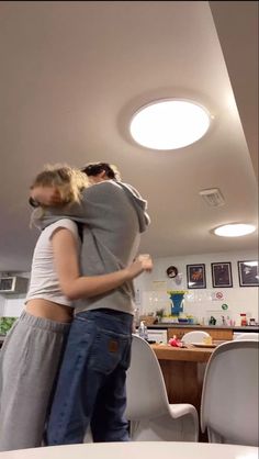 two people hugging each other while standing in a room with chairs and pictures on the wall