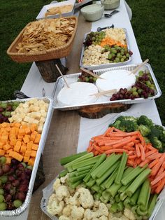 several trays of food on a table with grapes, celery, cauliflower and carrots