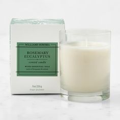 a candle sitting next to a box of rosemary eucalyptus scented candles on a white surface