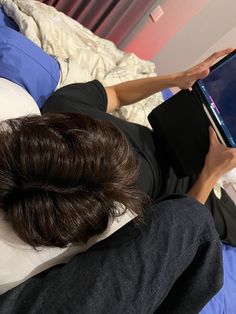 a person laying on a bed with a book in their hand and looking at the screen