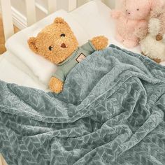 two teddy bears laying on top of a bed next to pillows and blankets in a crib