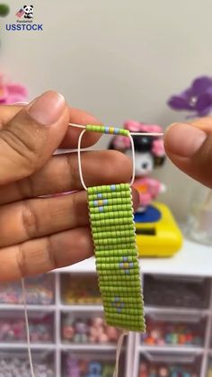 two hands are holding a piece of green beaded material in front of a shelf