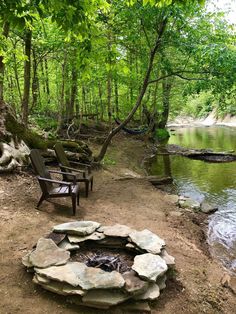 an outdoor fire pit in the middle of a wooded area with benches and chairs around it