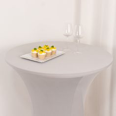 small desserts are placed on a plate on a white table with two wine glasses