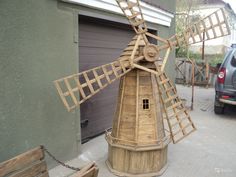 a wooden windmill sitting on top of a sidewalk next to a car parked in front of a garage