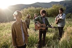 three men are standing in the grass with guitars and looking at something off to the side