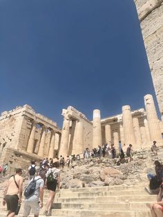 many people are walking up and down the stairs in front of an ancient building with columns