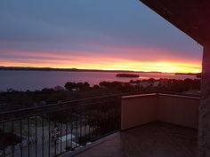 the sun is setting over some water and houses on the other side, as seen from an apartment balcony