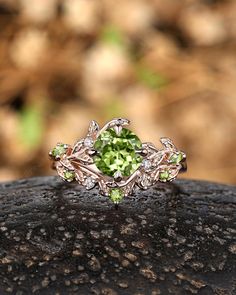 a green ring sitting on top of a black piece of rock with leaves around it